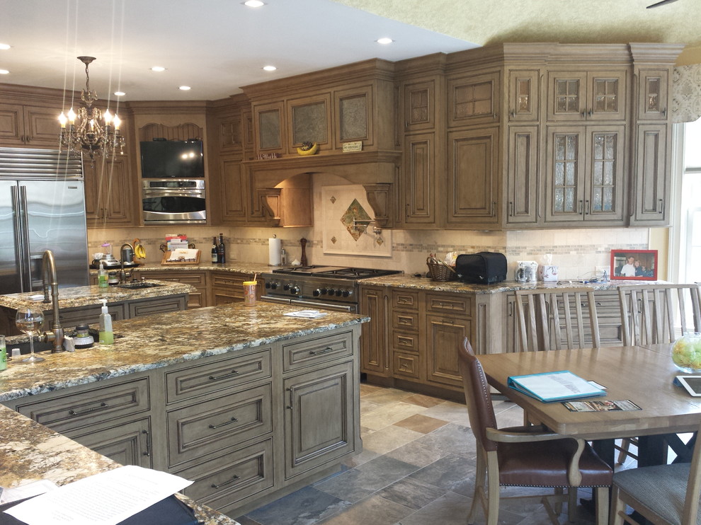 Inspiration for an expansive traditional l-shaped open plan kitchen in Philadelphia with an undermount sink, glass-front cabinets, distressed cabinets, granite benchtops, beige splashback, stone tile splashback, stainless steel appliances, porcelain floors and multiple islands.