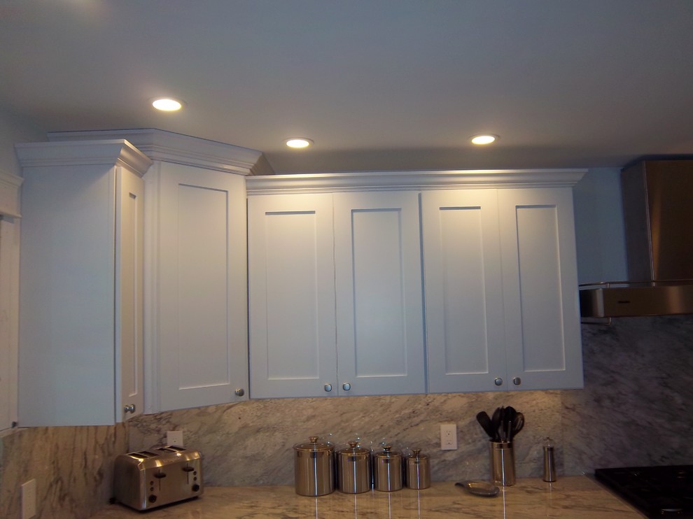 Example of a mid-sized transitional l-shaped medium tone wood floor and brown floor open concept kitchen design with an undermount sink, recessed-panel cabinets, white cabinets, granite countertops, gray backsplash, stone slab backsplash, stainless steel appliances and an island