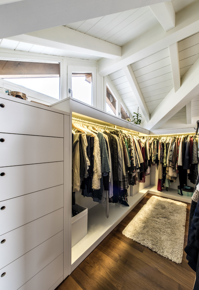 This is an example of a large transitional gender-neutral walk-in wardrobe in Milan with open cabinets, white cabinets, medium hardwood floors and brown floor.