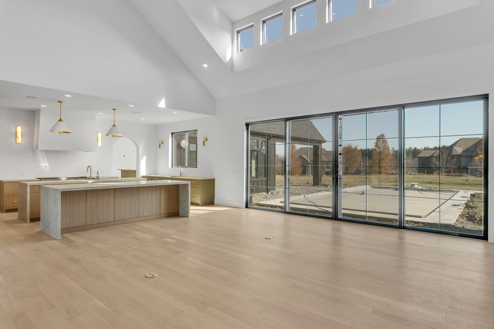 Inspiration for a large transitional u-shaped light wood floor, beige floor and vaulted ceiling open concept kitchen remodel with an undermount sink, flat-panel cabinets, light wood cabinets, quartzite countertops, white backsplash, paneled appliances, two islands and beige countertops