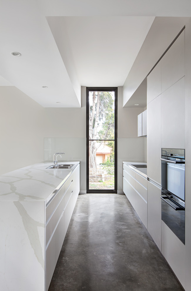 Design ideas for a mid-sized modern galley open plan kitchen in Melbourne with dark wood cabinets, marble benchtops, grey splashback, glass sheet splashback, concrete floors, with island, grey floor, white benchtop and vaulted.