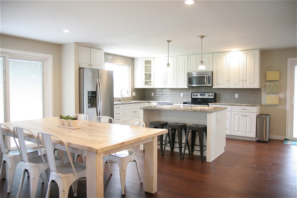 This is an example of a large country l-shaped eat-in kitchen in Boise with raised-panel cabinets, white cabinets, granite benchtops, grey splashback, porcelain splashback, stainless steel appliances, dark hardwood floors and with island.