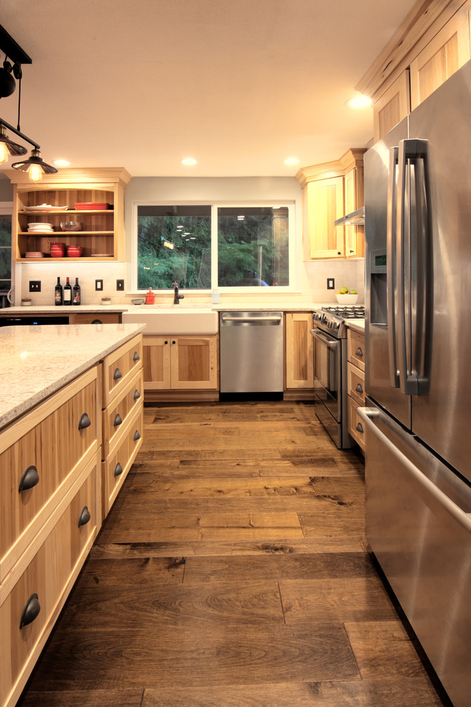 This is an example of a mid-sized country l-shaped eat-in kitchen in Seattle with a farmhouse sink, shaker cabinets, light wood cabinets, quartz benchtops, beige splashback, stone tile splashback, stainless steel appliances, medium hardwood floors, with island and brown floor.