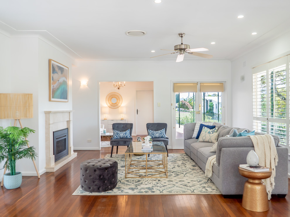 This is an example of a beach style formal living room in Other with white walls, medium hardwood floors, a standard fireplace, no tv and brown floor.