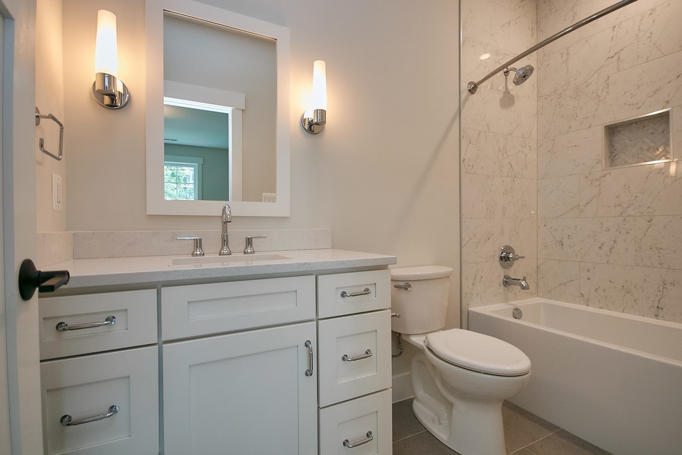 Photo of a mid-sized transitional kids bathroom in DC Metro with recessed-panel cabinets, white cabinets, an alcove tub, a shower/bathtub combo, a two-piece toilet, multi-coloured tile, marble, grey walls, ceramic floors, an undermount sink, engineered quartz benchtops, grey floor, a shower curtain and grey benchtops.