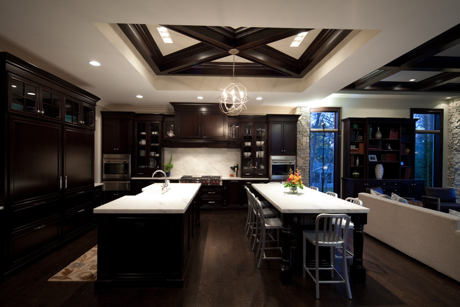 Design ideas for a large modern l-shaped open plan kitchen in Chicago with a farmhouse sink, recessed-panel cabinets, dark wood cabinets, marble benchtops, white splashback, stone slab splashback, panelled appliances, dark hardwood floors and multiple islands.