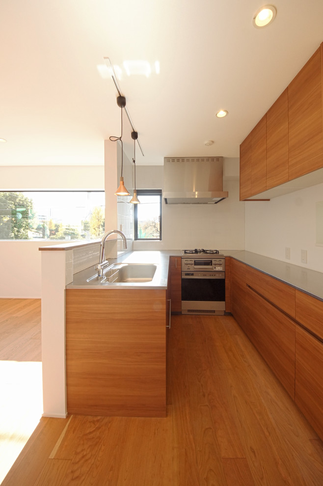 This is an example of a mid-sized modern u-shaped open plan kitchen in Tokyo with an integrated sink, flat-panel cabinets, medium wood cabinets, stainless steel benchtops, white splashback, medium hardwood floors and no island.