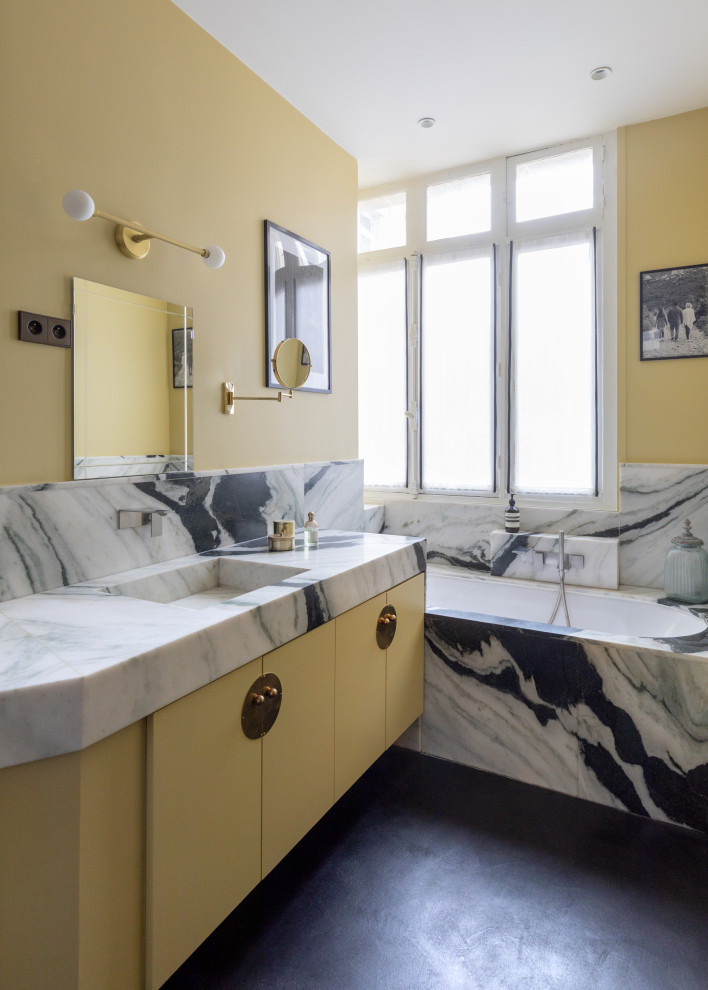 Idée de décoration pour une salle de bain design avec un placard à porte plane, des portes de placard jaunes, une baignoire encastrée, un mur jaune, sol en béton ciré, un lavabo intégré, un sol noir, un plan de toilette gris, meuble simple vasque et meuble-lavabo suspendu.