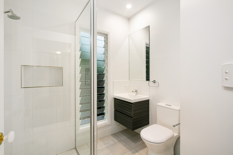 Inspiration for a small contemporary bathroom in Cairns with dark wood cabinets, a corner shower, a one-piece toilet, white tile, ceramic tile, white walls, cement tiles, an undermount sink, solid surface benchtops, beige floor, a hinged shower door, white benchtops, a single vanity and a floating vanity.