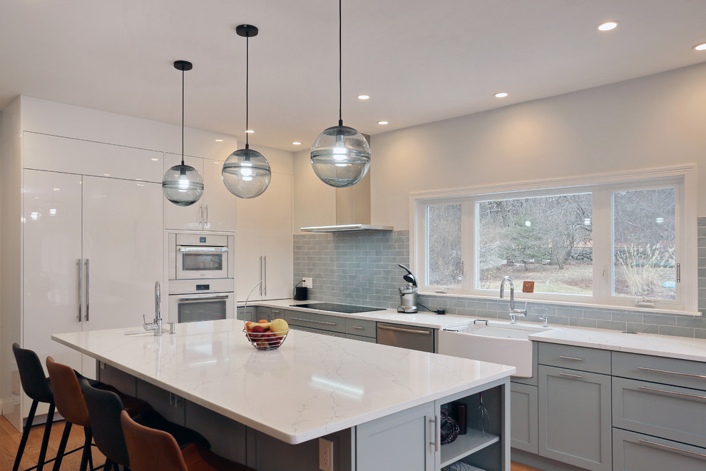 This is an example of a mid-sized transitional l-shaped kitchen in Boston with a farmhouse sink, shaker cabinets, grey cabinets, quartz benchtops, grey splashback, panelled appliances, with island, white benchtop, subway tile splashback and medium hardwood floors.