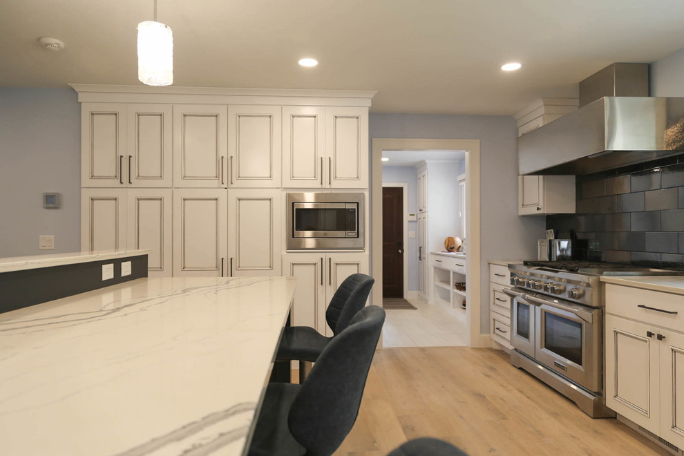 Eat-in kitchen - mid-sized transitional u-shaped light wood floor and beige floor eat-in kitchen idea with an undermount sink, recessed-panel cabinets, white cabinets, quartzite countertops, black backsplash, porcelain backsplash, stainless steel appliances, an island and white countertops