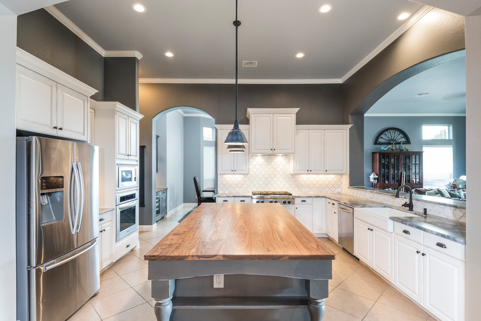 Photo of a large country u-shaped open plan kitchen in Austin with a farmhouse sink, raised-panel cabinets, distressed cabinets, marble benchtops, white splashback, ceramic splashback, stainless steel appliances, ceramic floors and with island.