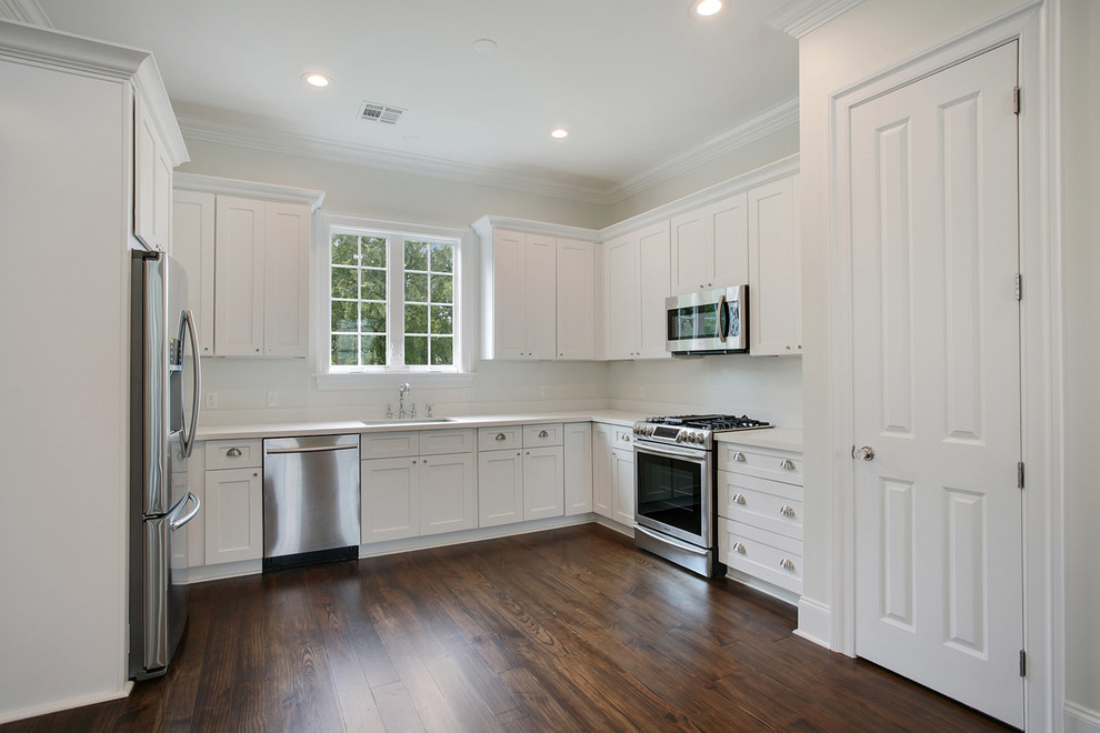 Small traditional l-shaped eat-in kitchen in New Orleans with flat-panel cabinets, white cabinets, white splashback, stainless steel appliances, dark hardwood floors and no island.