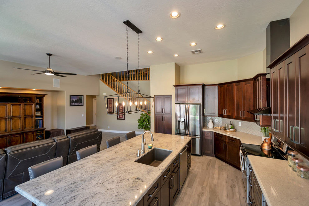 Inspiration for a mid-sized transitional l-shaped porcelain tile and brown floor open concept kitchen remodel in Phoenix with a single-bowl sink, shaker cabinets, brown cabinets, granite countertops, gray backsplash, brick backsplash, stainless steel appliances, an island and multicolored countertops