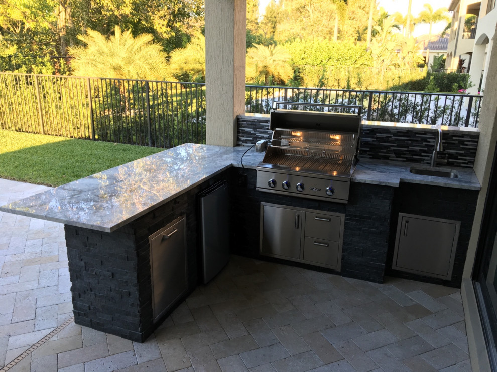 Photo of a large modern backyard patio in Miami with an outdoor kitchen, natural stone pavers and a roof extension.