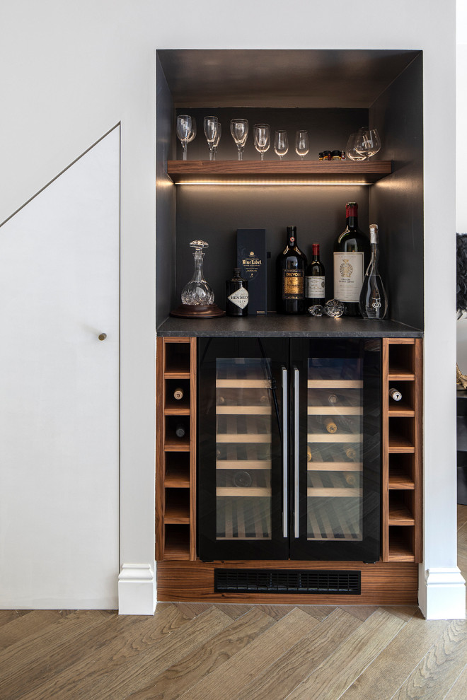Mid-sized transitional single-wall home bar in London with an integrated sink, shaker cabinets, green cabinets, soapstone benchtops, multi-coloured splashback, stone slab splashback, medium hardwood floors, brown floor and black benchtop.