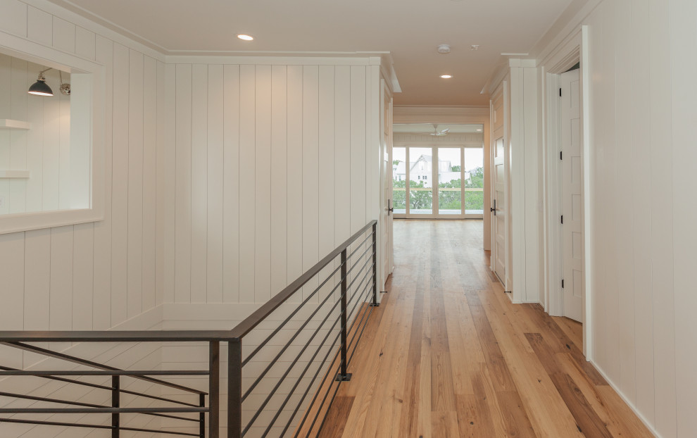 Photo of a large beach style wood u-shaped staircase in Charleston with painted wood risers, metal railing and planked wall panelling.