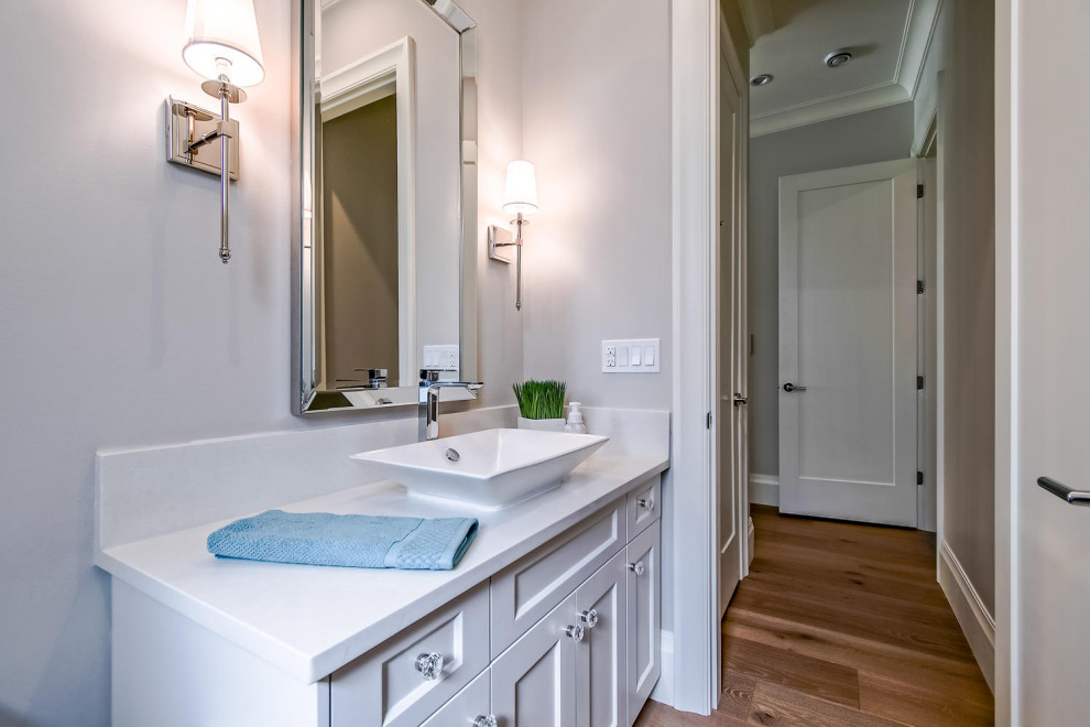 Powder room - mid-sized transitional medium tone wood floor and brown floor powder room idea in Vancouver with shaker cabinets, white cabinets, a one-piece toilet, gray walls, a vessel sink, quartz countertops, white countertops and a built-in vanity