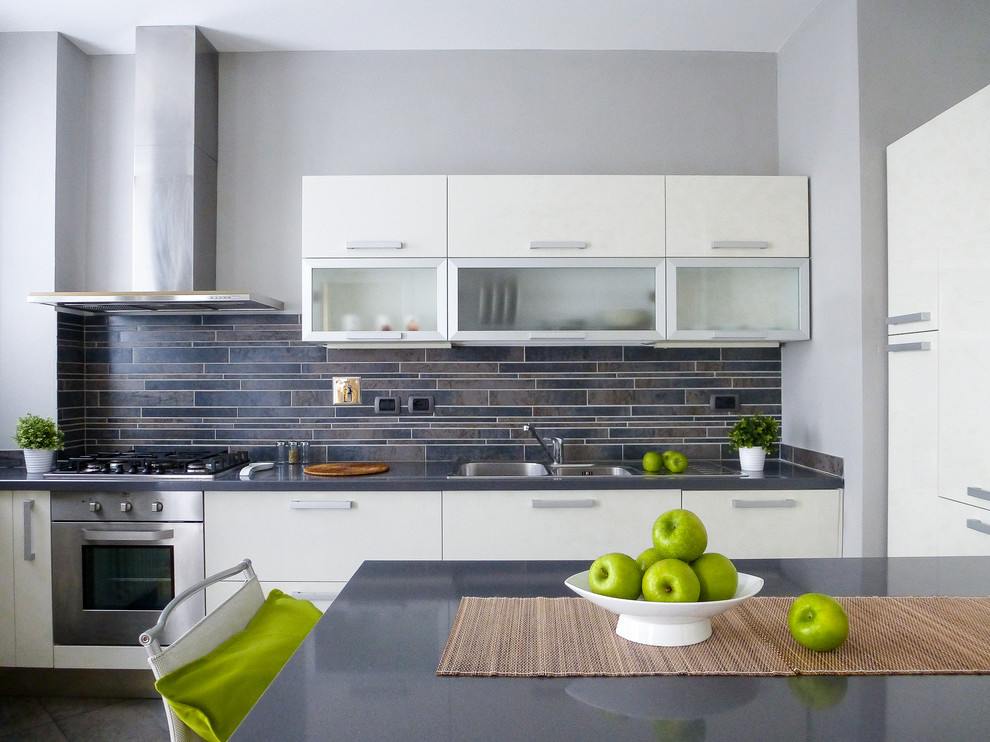 This is an example of a small contemporary single-wall eat-in kitchen in Florence with a double-bowl sink, flat-panel cabinets, stainless steel cabinets, black splashback, matchstick tile splashback, stainless steel appliances and grey floor.