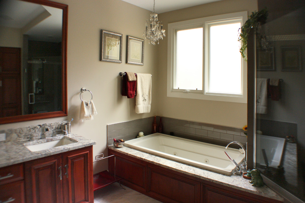 This is an example of a large traditional master bathroom in Grand Rapids with raised-panel cabinets, medium wood cabinets, a corner tub, a corner shower, a two-piece toilet, multi-coloured tile, porcelain tile, beige walls, porcelain floors, an undermount sink and granite benchtops.