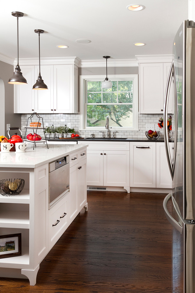 Inspiration for a traditional kitchen in Minneapolis with recessed-panel cabinets, white cabinets, white splashback, subway tile splashback, stainless steel appliances and brown floor.