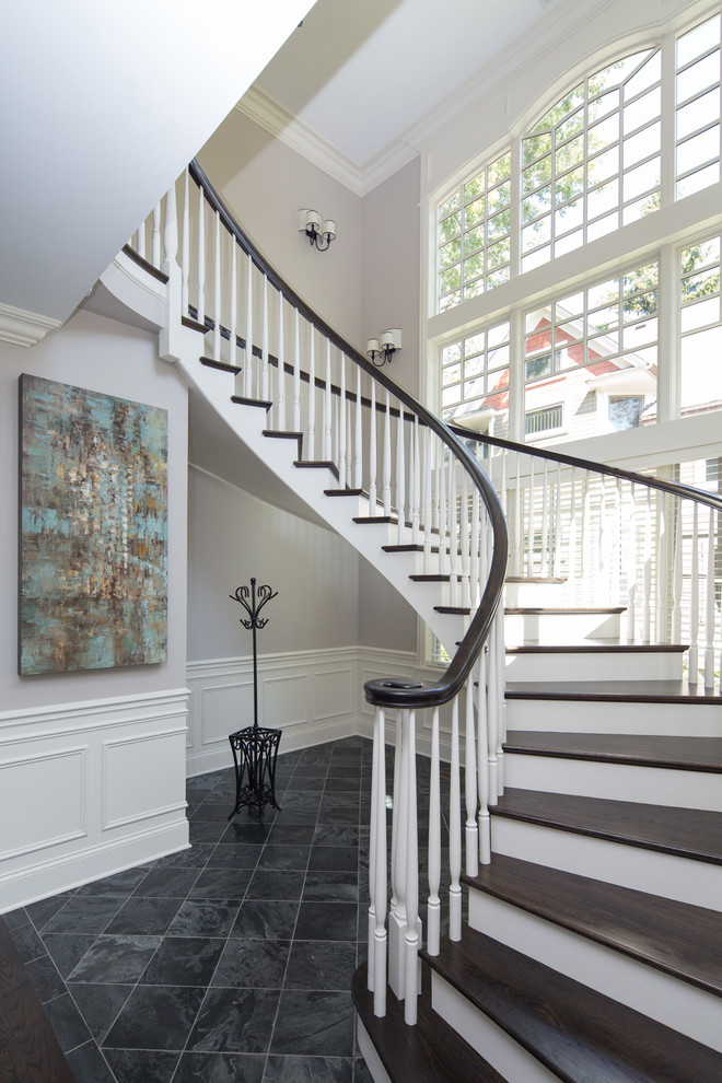 This is an example of a large traditional wood curved staircase in Chicago with painted wood risers.