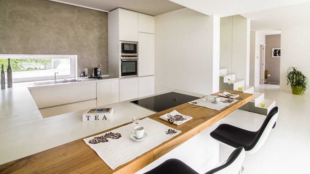 This is an example of a large contemporary u-shaped open plan kitchen in Other with a drop-in sink, flat-panel cabinets, white cabinets, grey splashback, stainless steel appliances and a peninsula.