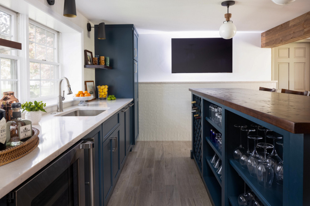 This is an example of a traditional wet bar in Boston with a submerged sink, flat-panel cabinets, blue cabinets, wood worktops, white splashback, ceramic splashback, porcelain flooring, brown floors and brown worktops.