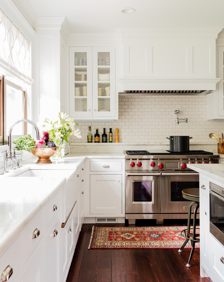 Inspiration for a large traditional l-shaped kitchen in Boston with a farmhouse sink, white cabinets, marble benchtops, white splashback, subway tile splashback, dark hardwood floors, with island, shaker cabinets and stainless steel appliances.