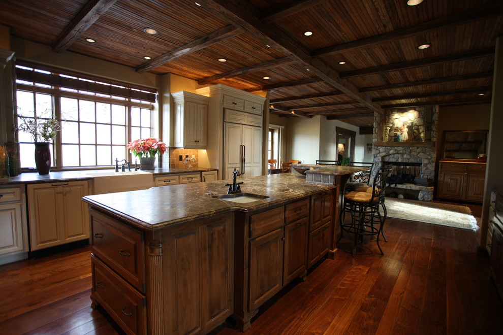 Example of a large mountain style l-shaped medium tone wood floor and brown floor open concept kitchen design with an undermount sink, white cabinets, granite countertops, brown backsplash, stone tile backsplash, stainless steel appliances and an island