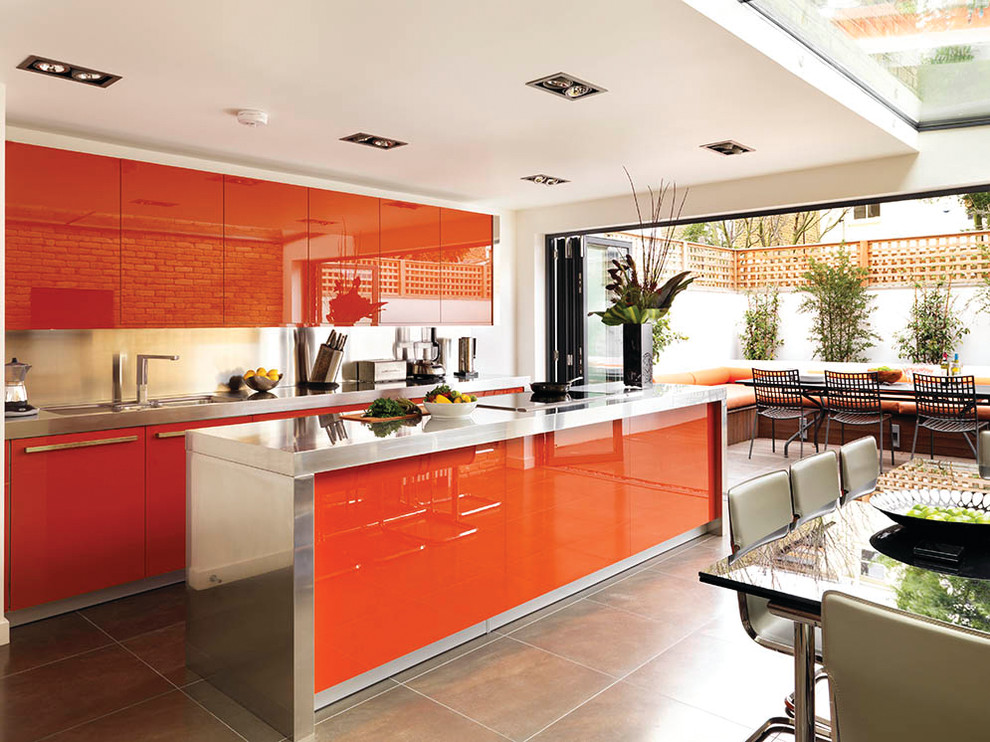 This is an example of a contemporary eat-in kitchen in London with an integrated sink, flat-panel cabinets, stainless steel benchtops, porcelain floors, with island and orange cabinets.