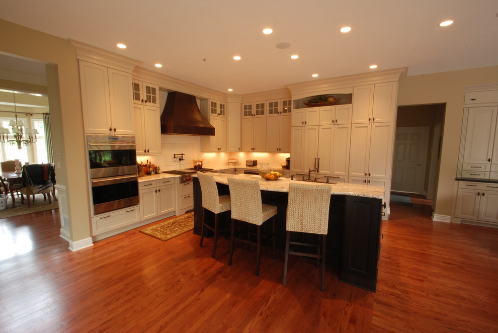 Eat-in kitchen - large transitional l-shaped medium tone wood floor eat-in kitchen idea with a farmhouse sink, recessed-panel cabinets, light wood cabinets, granite countertops, white backsplash, stainless steel appliances and an island