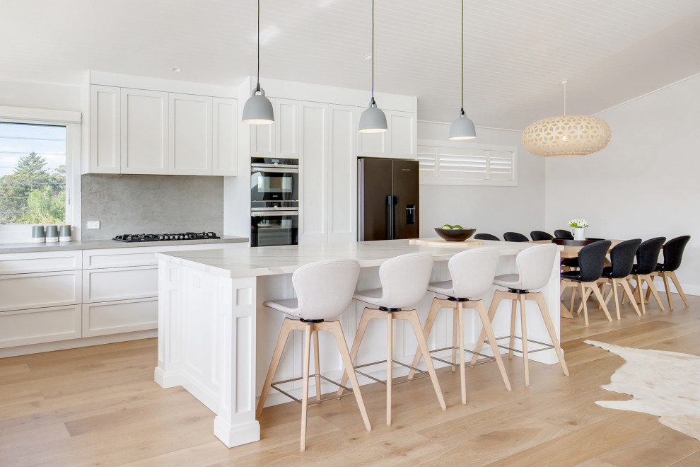 Design ideas for a large beach style l-shaped open plan kitchen in Sydney with a drop-in sink, shaker cabinets, white cabinets, quartz benchtops, multi-coloured splashback, engineered quartz splashback, stainless steel appliances, light hardwood floors, with island, multi-coloured floor and multi-coloured benchtop.
