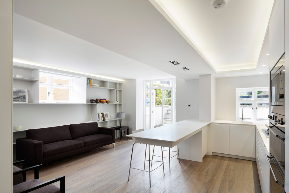 Inspiration for a contemporary u-shaped open plan kitchen in London with an integrated sink, flat-panel cabinets, white cabinets, stainless steel appliances, medium hardwood floors and a peninsula.