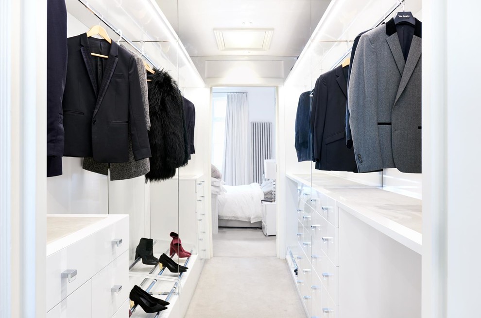 Photo of a contemporary gender-neutral walk-in wardrobe in London with open cabinets, white cabinets, carpet and beige floor.