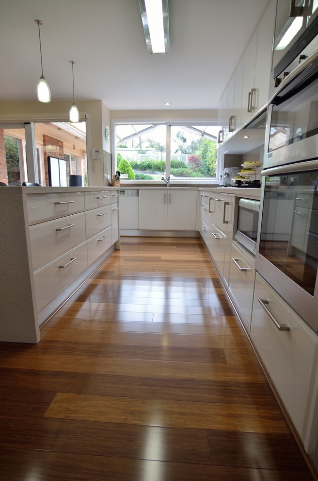 Large modern l-shaped eat-in kitchen in Melbourne with a double-bowl sink, open cabinets, white cabinets, granite benchtops, brown splashback, glass sheet splashback, stainless steel appliances, bamboo floors and with island.