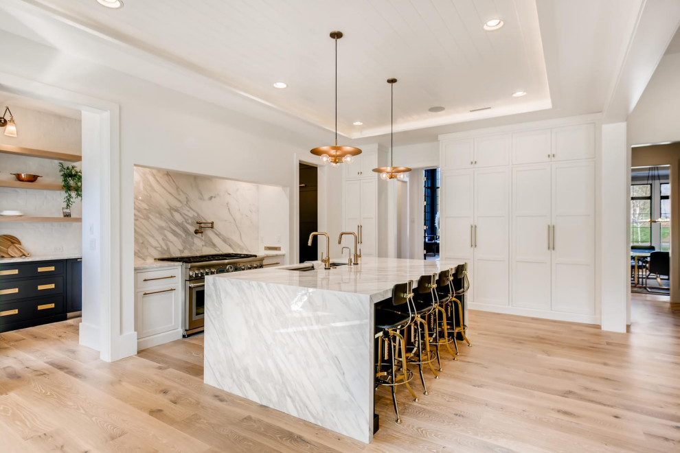 This is an example of a large modern l-shaped eat-in kitchen in Denver with a drop-in sink, flat-panel cabinets, white cabinets, marble benchtops, white splashback, marble splashback, stainless steel appliances, light hardwood floors, with island and white benchtop.