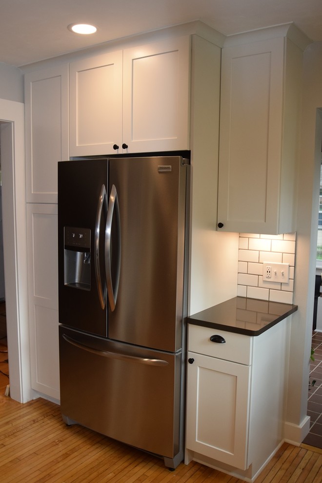 Inspiration for a transitional u-shaped light wood floor kitchen remodel with an undermount sink, shaker cabinets, white cabinets, quartz countertops, white backsplash, subway tile backsplash, stainless steel appliances, no island and black countertops