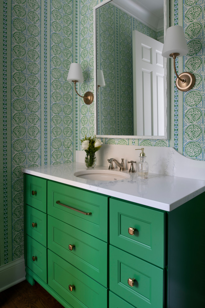 Photo of a medium sized nautical cloakroom in Minneapolis with recessed-panel cabinets, green cabinets, a one-piece toilet, green tiles, multi-coloured walls, dark hardwood flooring, a submerged sink, marble worktops, brown floors, white worktops, a built in vanity unit and wallpapered walls.