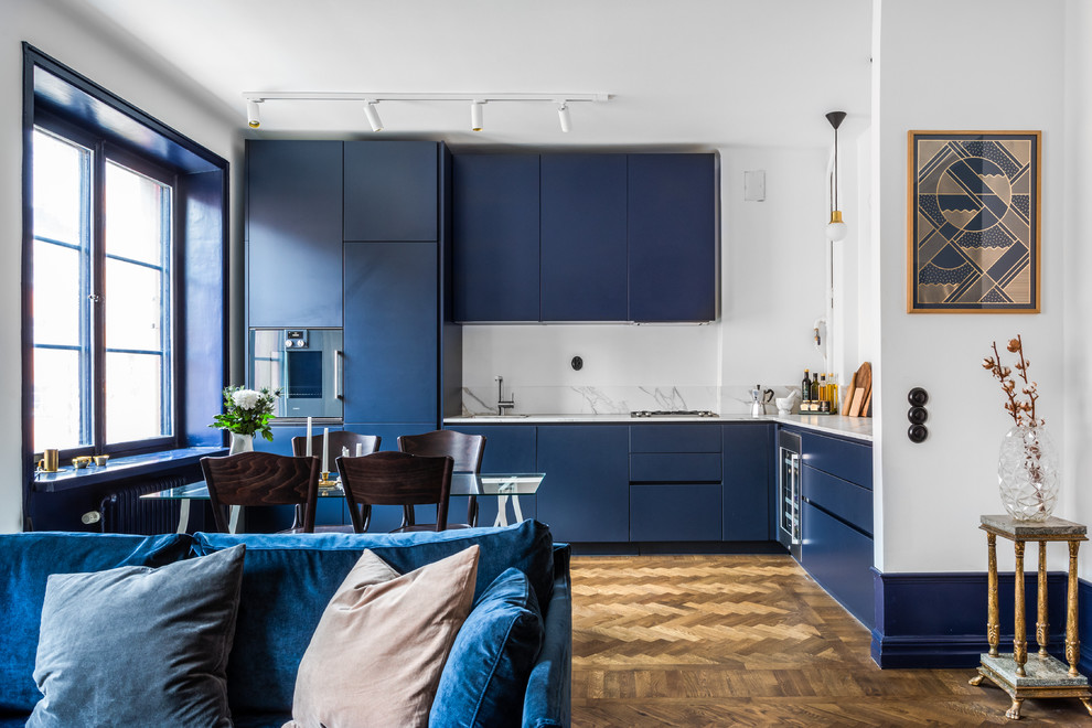 Scandinavian l-shaped open plan kitchen in Stockholm with flat-panel cabinets, blue cabinets, grey splashback, stainless steel appliances, medium hardwood floors, no island and brown floor.