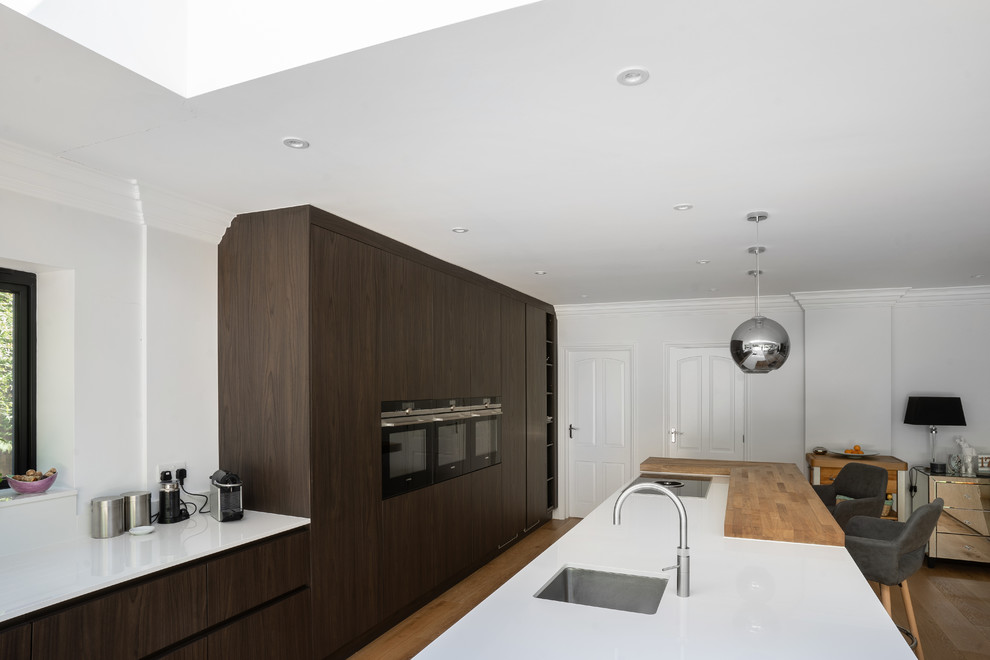 Inspiration for a large contemporary galley open plan kitchen in Essex with an integrated sink, flat-panel cabinets, brown cabinets, quartzite benchtops, panelled appliances, medium hardwood floors, with island, brown floor and white benchtop.