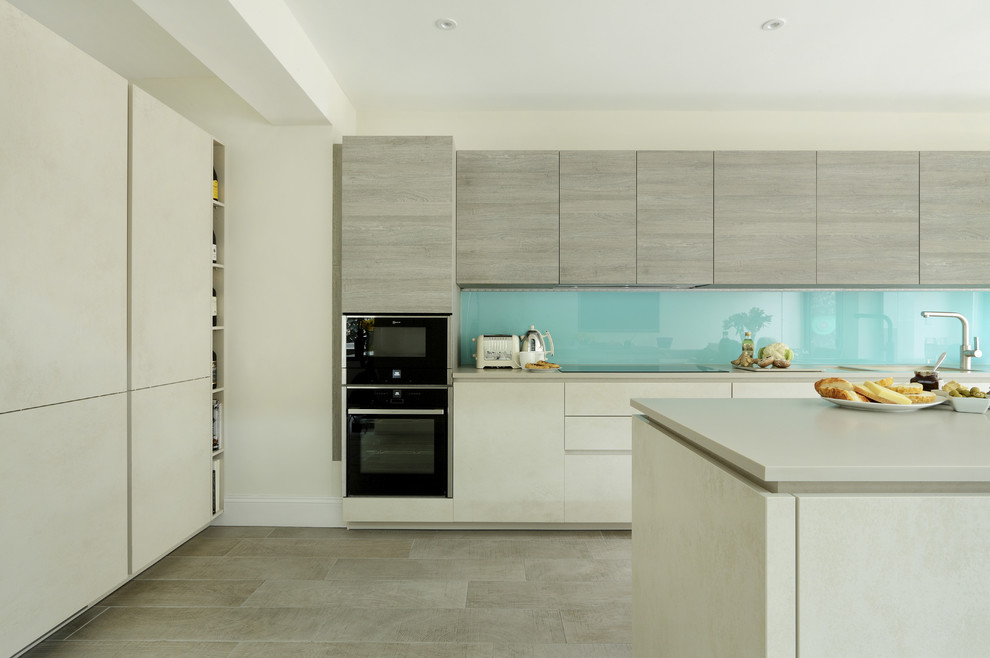 Photo of a contemporary l-shaped kitchen in London with flat-panel cabinets, grey cabinets, blue splashback, black appliances, with island and grey floor.