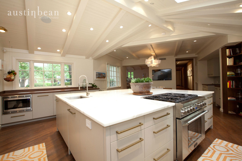Example of a large transitional u-shaped medium tone wood floor eat-in kitchen design with an integrated sink, flat-panel cabinets, white cabinets, stainless steel countertops, white backsplash, stone slab backsplash, stainless steel appliances and white walls