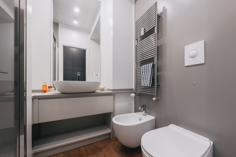Exempel på ett litet modernt grå grått badrum med dusch, med släta luckor, vita skåp, en dusch i en alkov, en toalettstol med separat cisternkåpa, grå kakel, porslinskakel, flerfärgade väggar, mörkt trägolv, ett fristående handfat, bänkskiva i akrylsten, brunt golv och dusch med skjutdörr