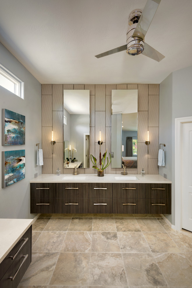 This is an example of a contemporary bathroom in Phoenix with flat-panel cabinets, medium wood cabinets, a two-piece toilet, gray tile, porcelain tile, grey walls, porcelain floors, a drop-in sink and solid surface benchtops.