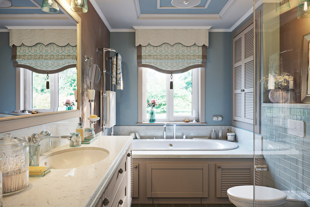 Design ideas for a mid-sized country master bathroom in Moscow with louvered cabinets, a drop-in tub, a wall-mount toilet, blue tile, ceramic tile, blue walls, ceramic floors, an undermount sink, marble benchtops, brown floor, a hinged shower door, beige benchtops and beige cabinets.