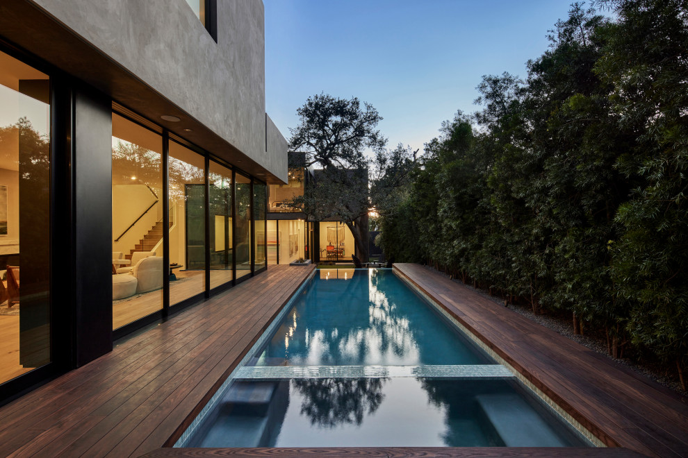 Diseño de piscina infinita minimalista grande rectangular en patio lateral con paisajismo de piscina y entablado