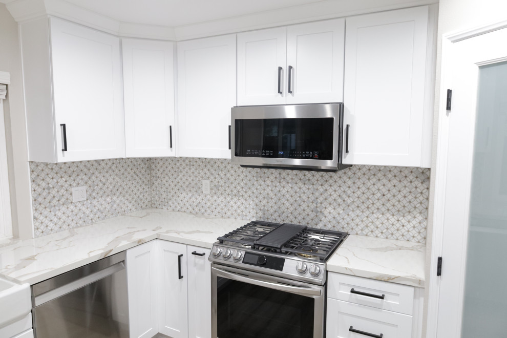 This is an example of a mid-sized modern eat-in kitchen in San Diego with a farmhouse sink, shaker cabinets, white cabinets, quartz benchtops, white splashback, mosaic tile splashback, stainless steel appliances, laminate floors, a peninsula, grey floor and white benchtop.
