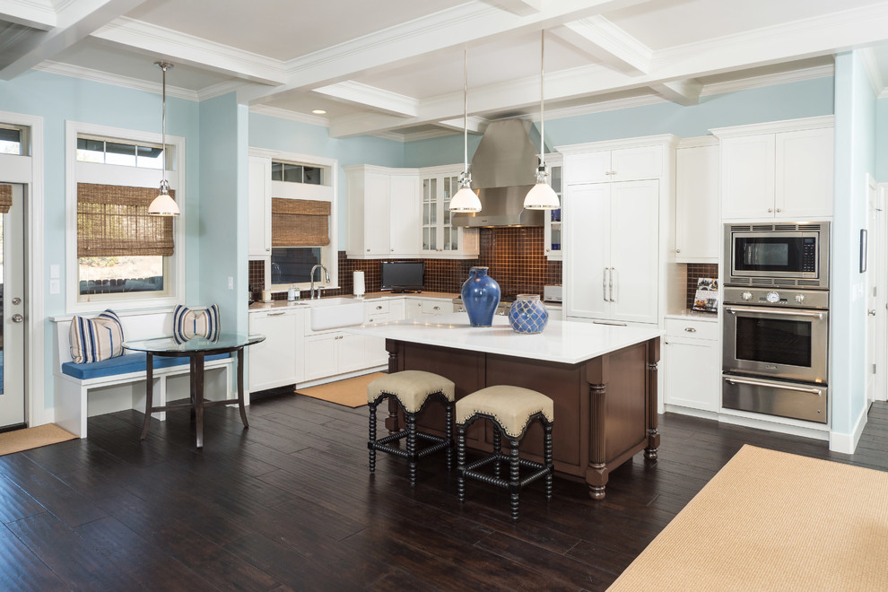 Mid-sized transitional l-shaped dark wood floor and brown floor enclosed kitchen photo with a farmhouse sink, shaker cabinets, white cabinets, quartzite countertops, brown backsplash, mosaic tile backsplash, stainless steel appliances, an island and white countertops