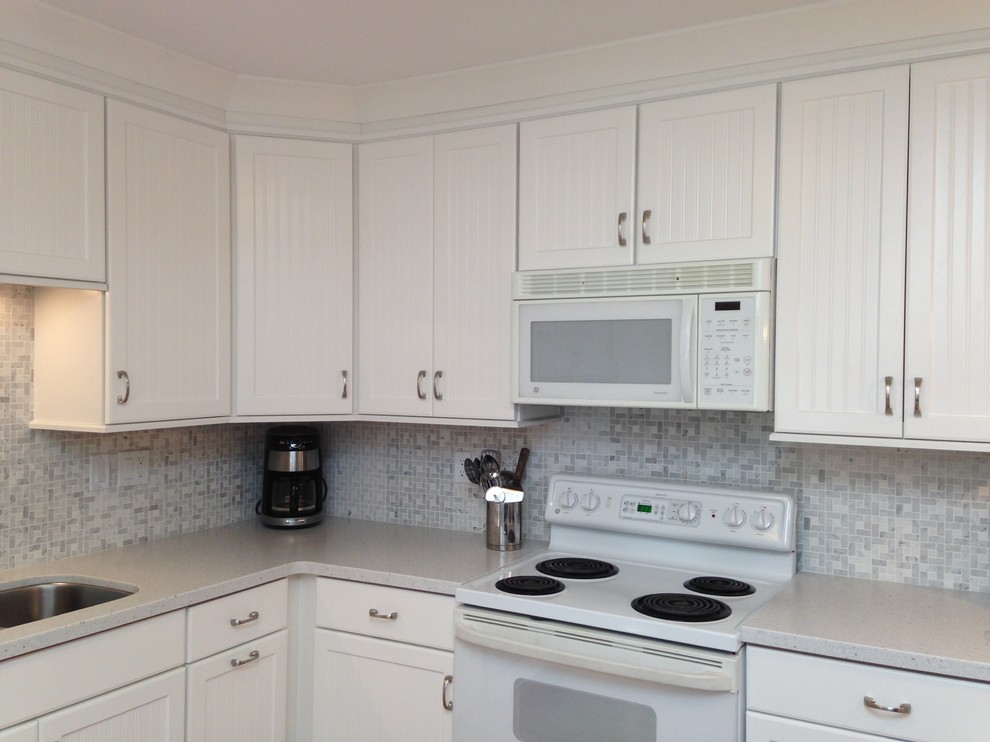 Example of a mid-sized beach style l-shaped eat-in kitchen design with an undermount sink, beaded inset cabinets, white cabinets, solid surface countertops, gray backsplash, mosaic tile backsplash, white appliances and a peninsula
